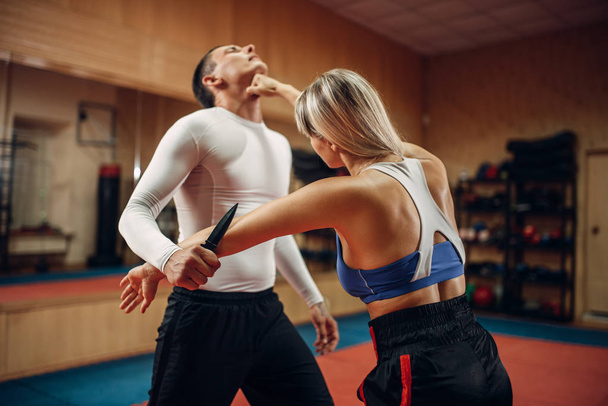 Woman makes punch to the throat, self-defense workout with male personal trainer, gym interior on background. Female person on training, self defense practice - Fotó, kép