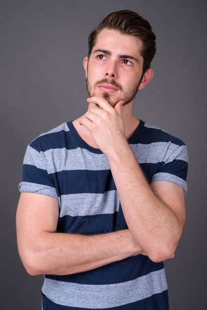 Young handsome bearded man against gray background - Foto, afbeelding