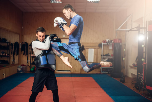 Hombre kickboxer haciendo patada en salto, practicando con un entrenador personal, entrenamiento en el gimnasio. Boxeador en entrenamiento, práctica de kickboxing
 - Foto, imagen