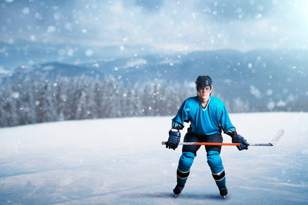 Un giocatore di hockey con bastone su ghiaccio aperto, concetto di gioco, foresta innevata sullo sfondo. Uomo in casco, guanti e uniforme protettiva all'aperto, gioco di sport invernali
 - Foto, immagini