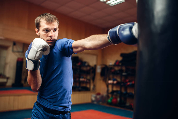 Male kickboxer hits the punching bag on workout in gym. Boxer practicing strikes on training, kickboxing practice - Photo, Image