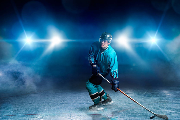 ein Eishockeyspieler auf dem Eis, Scheinwerfer im Hintergrund. männliche Person mit Helm, Handschuhen und Uniform hält Stock in den Händen - Foto, Bild