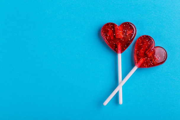 Two red sweet tasty lollipops in shape of heart on bright blue background. St. Valentine's day. Copy space - Fotografie, Obrázek