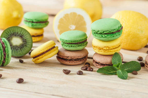 Green and yellow french macarons with kiwi, lemon and mint decorations, soft focus background - Zdjęcie, obraz