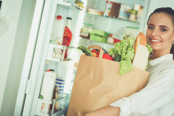 Mladá žena drží nákupní tašku s potravinami se zeleninou.Stojící v kuchyni - Fotografie, Obrázek