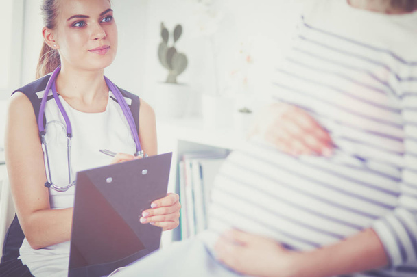 Молода жінка-лікар зі стетоскопом і планшетом розмовляє з вагітною жінкою в лікарні
. - Фото, зображення