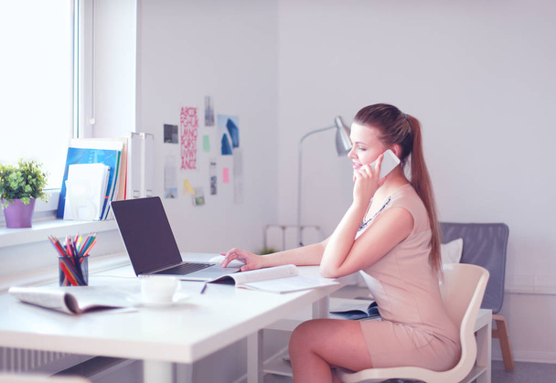 Young businesswoman sitting at the desk and talking on phone - Photo, image