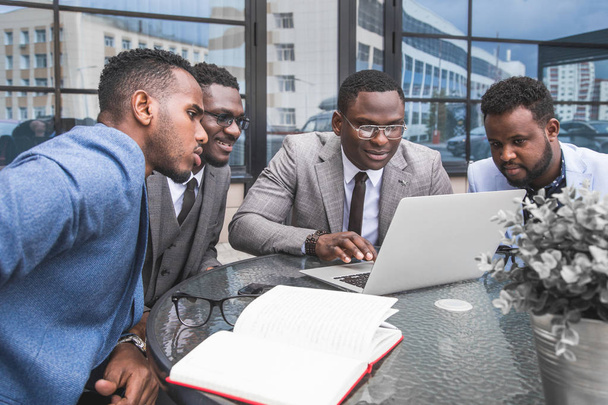 Group of happy diverse male and female business people team in formal gathered around laptop computer in bright office against the background of a glass building - Photo, image