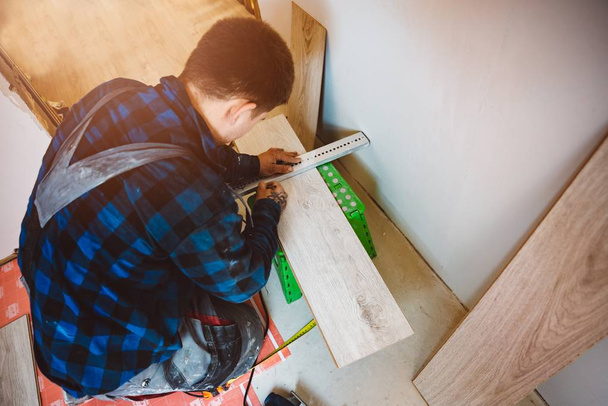 Працівник вимірює і маркує плитку для ламінованої підлоги для різання, встановлення ламінованих підлог. Концепція благоустрою та реконструкції будинку
 - Фото, зображення