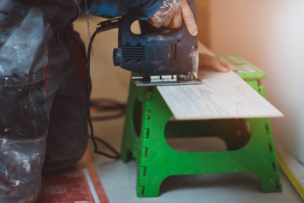 Trabalhador de instalação de painéis de piso laminado e painéis de corte com serra elétrica. Melhoria da casa e conceito de renovação
 - Foto, Imagem