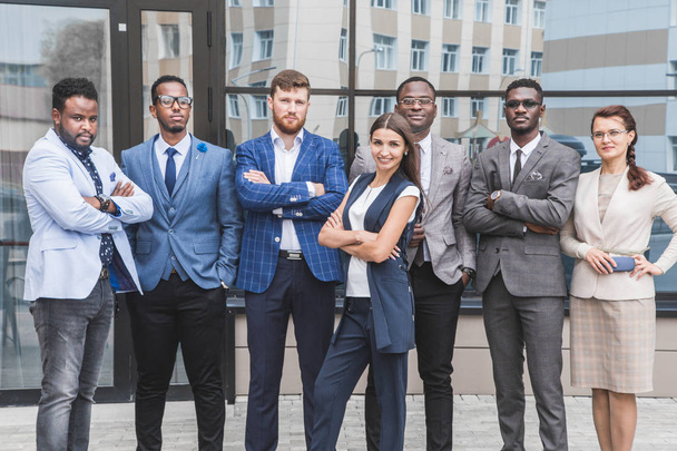 Successful company with happy workers. Men and women in business suits stand with their arms crossed against the background of skyscrapers - Foto, Imagen
