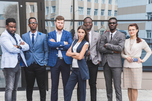 Successful company with happy workers. Men and women in business suits stand with their arms crossed against the background of skyscrapers - Foto, immagini