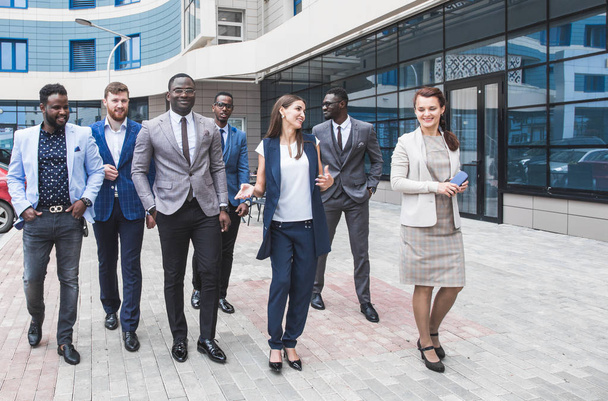 Successful company with happy workers. Men and women in business suits stand with their arms crossed against the background of skyscrapers - Foto, immagini