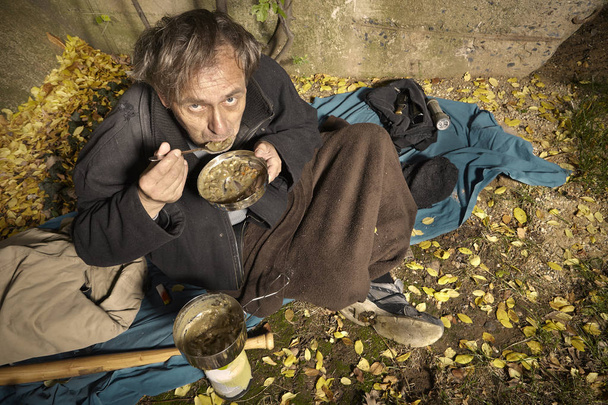 Ugly pauper man living outdoor preparing and eating lentil soup - Foto, imagen