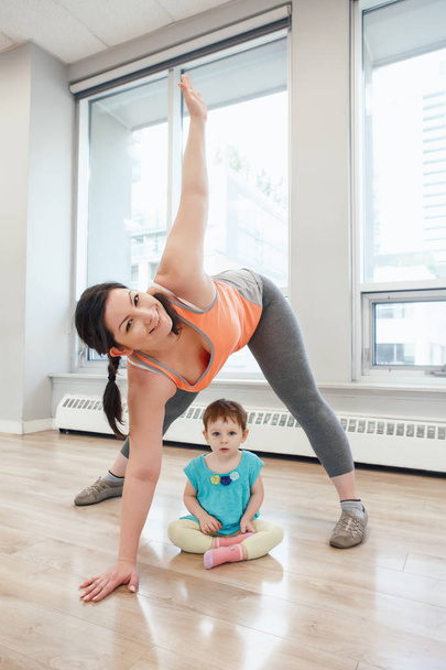 Νεαρή γυναίκα με το παιδί να κάνει προπόνηση στην τάξη γυμναστήριο χαλαρά μωρό βάρους. Γυμναστήριο οικογένειες για τις μητέρες με παιδιά νήπια. Lifestyle έννοια της δραστηριότητας της μητρικής.  - Φωτογραφία, εικόνα