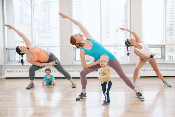 A csoport három fiatal nő gyerekekkel csinál edzés edzőterem oktató laza baba súlya osztály. Gyermekbarát fitness anyák kisgyermekek gyerekek. Életmód fogalom szülő tevékenység - Fotó, kép