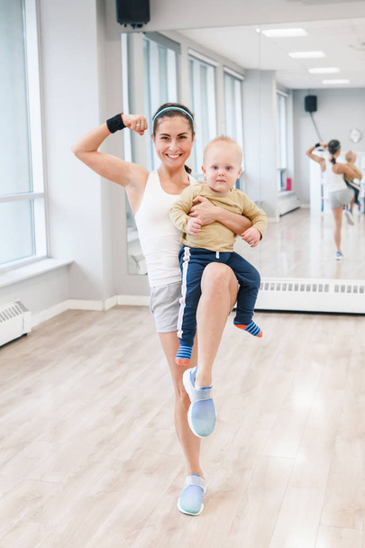 junge Frau mit Kind beim Workout in der Gymnastikstunde, um Gewicht zu verlieren. Kinderfreundliche Fitness für Mütter mit Kleinkindern. Lifestyle-Konzept der Elternaktivität.  - Foto, Bild