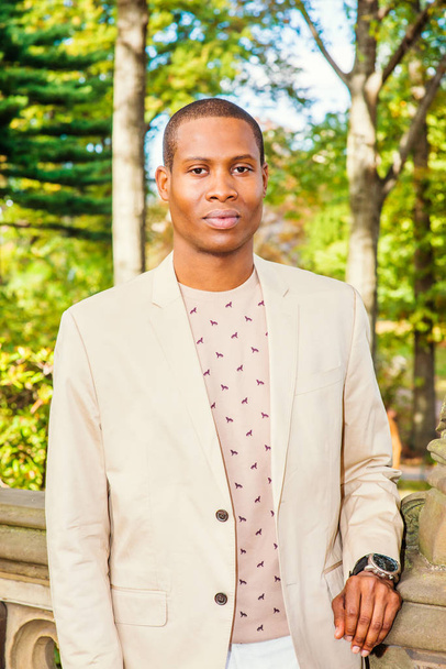 Retrato de un joven afroamericano en Nueva York. Vestirse con chaqueta de crema, suéter sin cuello, reloj de pulsera, un joven estudiante negro graduado está de pie en el campus, en serio mirándote
 - Foto, Imagen