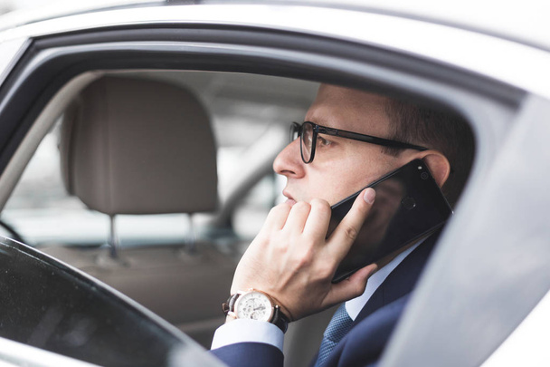 young successful businessman talking on the phone sitting in the back seat of an elite car, talks and business meetings - Фото, зображення