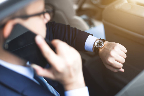 молодой успешный бизнесмен разговаривает по телефону сидя на заднем сиденье элитного автомобиля, переговоры и деловые встречи
 - Фото, изображение