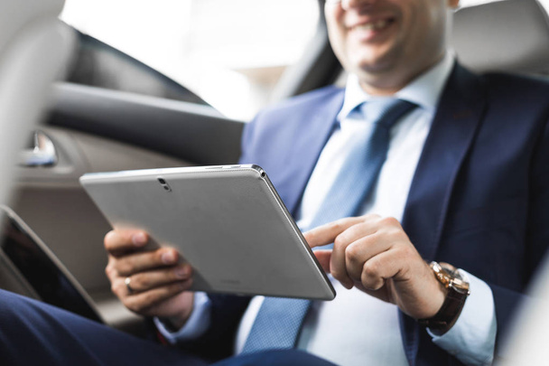 Jonge zakenman met behulp van tablet pc zittend op de achterbank van een auto. Kaukasische mannelijke zakelijke uitvoerende door een taxi en kijken naar digitale tablet. - Foto, afbeelding