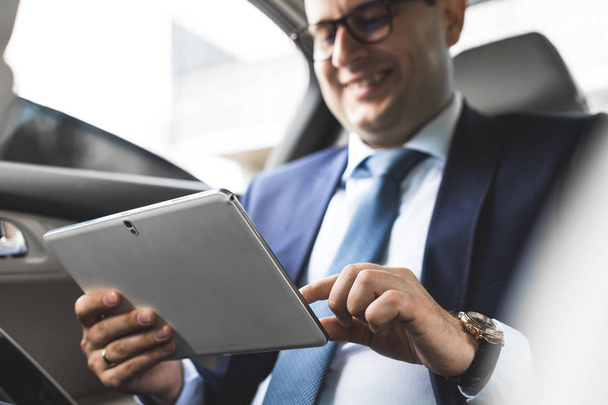 Young businessman using tablet pc while sitting on back seat of a car. Caucasian male business executive by a taxi and looking at digital tablet. - Fotoğraf, Görsel
