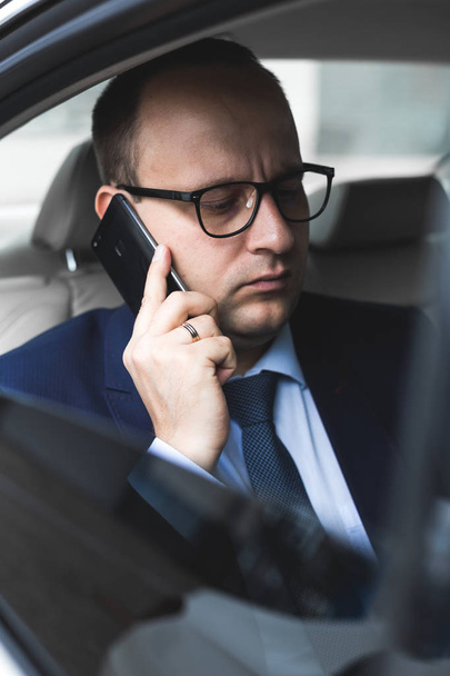 young successful businessman talking on the phone sitting in the back seat of an elite car, talks and business meetings - Fotoğraf, Görsel