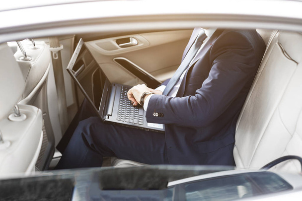a young business man in a suit is sitting in the back seat of a business car with a laptop and a notebook, business negotiations - Fotó, kép