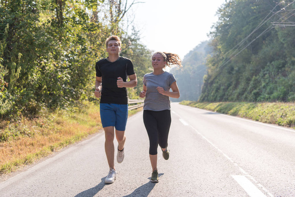 jovem casal desfrutando de um estilo de vida saudável enquanto corre ao longo de uma estrada rural, exercício e conceito de fitness - Foto, Imagem