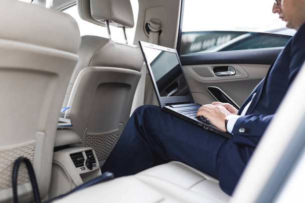 a young business man in a suit is sitting in the back seat of a business car with a laptop and a notebook, business negotiations - Foto, Imagem