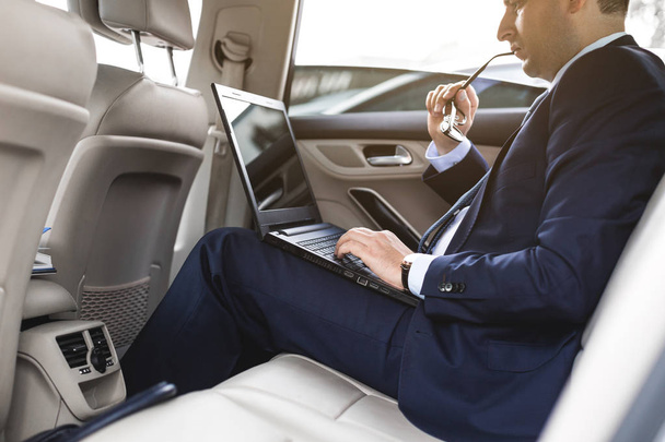 a young business man in a suit is sitting in the back seat of a business car with a laptop and a notebook, business negotiations - Fotografie, Obrázek