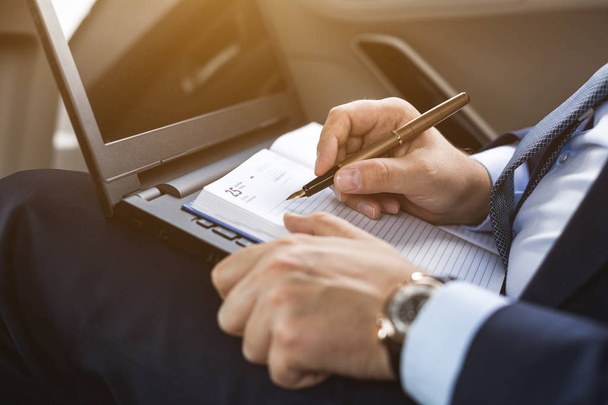 a young business man in a suit is sitting in the back seat of a business car with a laptop and a notebook, business negotiations - Photo, image
