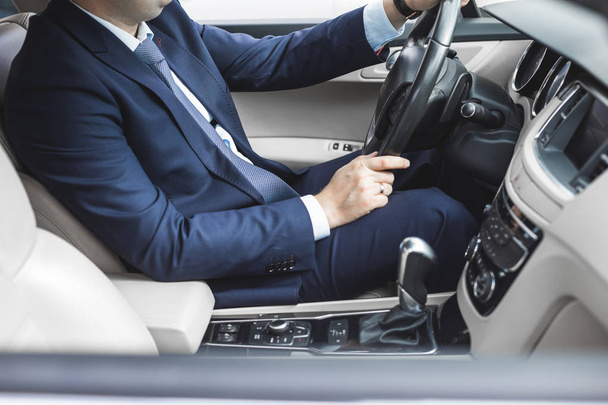 Ein Geschäftsmann am Steuer eines Prestigeautos hält ein Mobiltelefon in der Hand. Überstürztes Leben - Foto, Bild