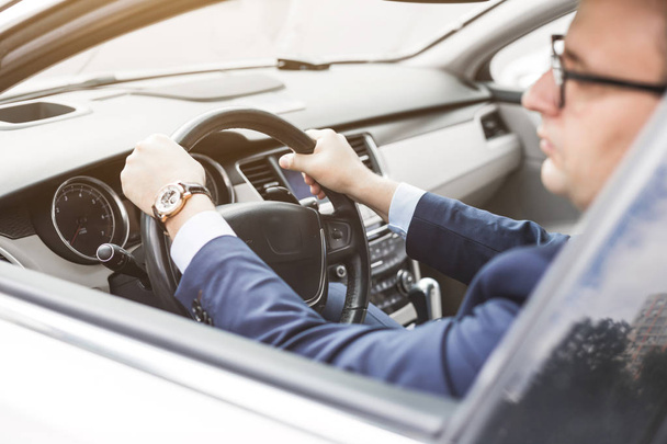een zakenman die een prestigieuze auto rijden houdt een mobiele telefoon in zijn hand. Haastige leven - Foto, afbeelding