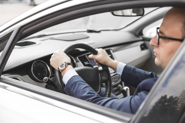 a businessman driving a prestigious car holds a mobile phone in his hand. Hasty life - Foto, immagini