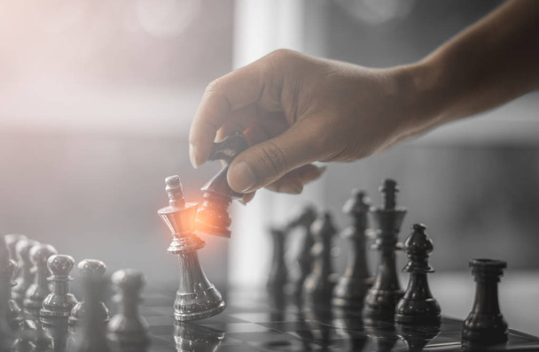 Стратегия деловой конкуренции и концепция успеха бизнеса. Рука двух бизнесменов движется для борьбы с темной шахматной фигурой короля на шахматной доске
. - Фото, изображение