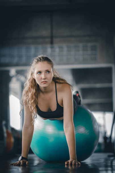 Ελκυστική νεαρή γυναίκα γυμναστήριο κάνει δύσκολο δύσκολο σανίδα την μπάλα στην προπόνηση γυμναστήριο. Γυναίκα τέντωμα των μυών και χαλάρωση μετά από άσκηση στο γυμναστήριο γυμναστήριο. - Φωτογραφία, εικόνα