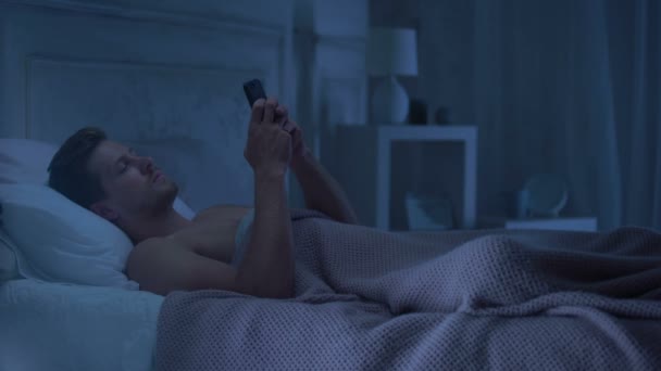 Man lying in bed chatting on phone, turning away from lady in seductive lingerie - Footage, Video