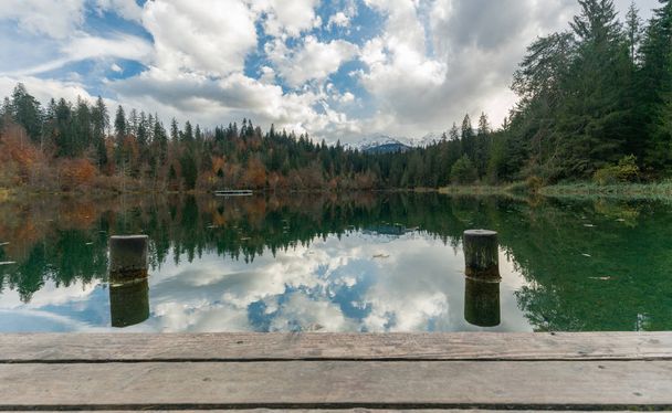 wooden pier and boardwalk with dock pylons on the edge of an idyllic mountain lake surrounded by fall color forest - Photo, Image