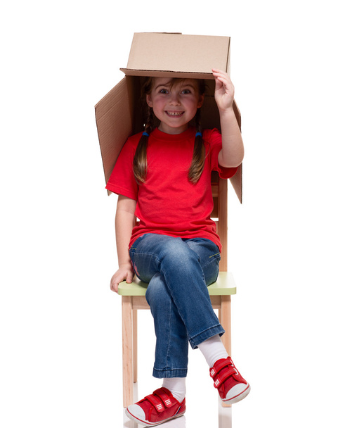 child sitting on a chair with big box covered head - Фото, изображение
