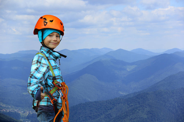 Portrait d'un garçon souriant de six ans portant un casque et un harnais de sécurité dans les montagnes, montrant comme un geste symbolique, un espace négatif
 - Photo, image