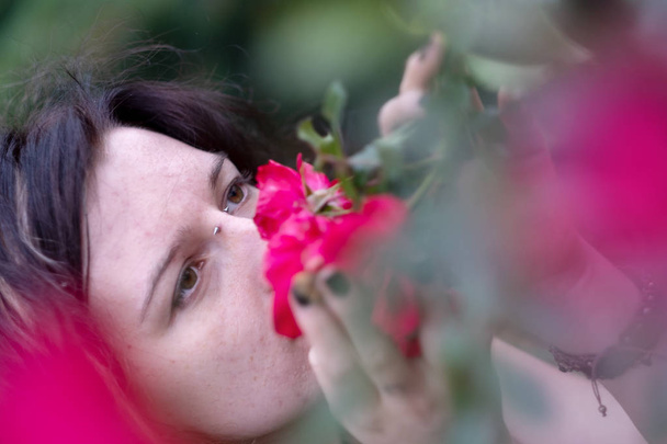 Egy gyönyörű fiatal egyedi, különc sötét hajú nő portréja, orrát megragadt mélyen a nő a kertben, a parkban, illatos vörös rózsa - Fotó, kép