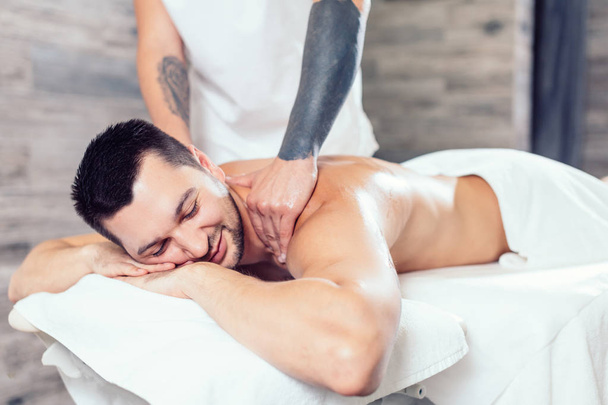 молодой позитивный человек наслаждается массажем в спа-центре
 - Фото, изображение