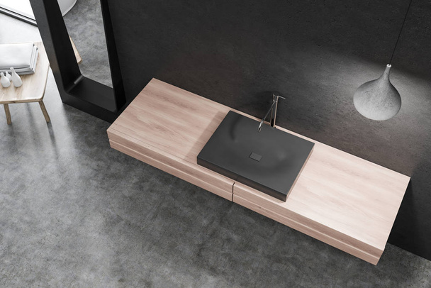Top view of black bathroom sink standing on wooden countertop in room with black walls and stylish ceiling lamp. 3d rendering - Foto, Bild
