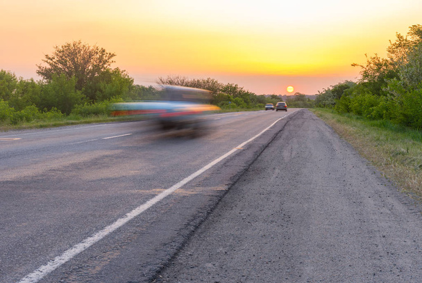 Puesta de sol sobre carretera rural con coches veloces corriendo al sol
 - Foto, Imagen