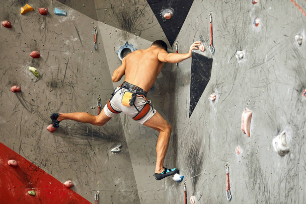 Male climber exercising in gym, climbing up on artificial wall with boulders. - Фото, зображення