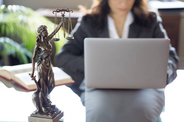 Oficina de abogados. Estatua de Justicia con escalas y abogado trabajando en un portátil
. - Foto, Imagen