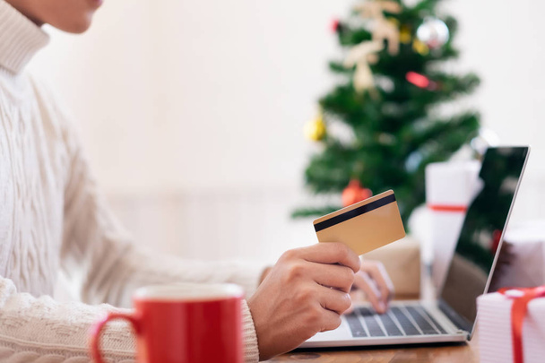 Чоловік тримає кредитну картку і здійснює покупки в Інтернеті. Новий рік, різдвяні покупки подарунків
 - Фото, зображення