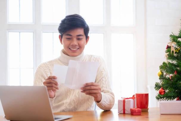 Christmas concept. Man wearing white sweater opening and sending christmas card. - Photo, Image