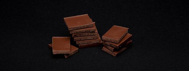 Chocolate blocks stack on black background, copyspace for your text. - Фото, изображение